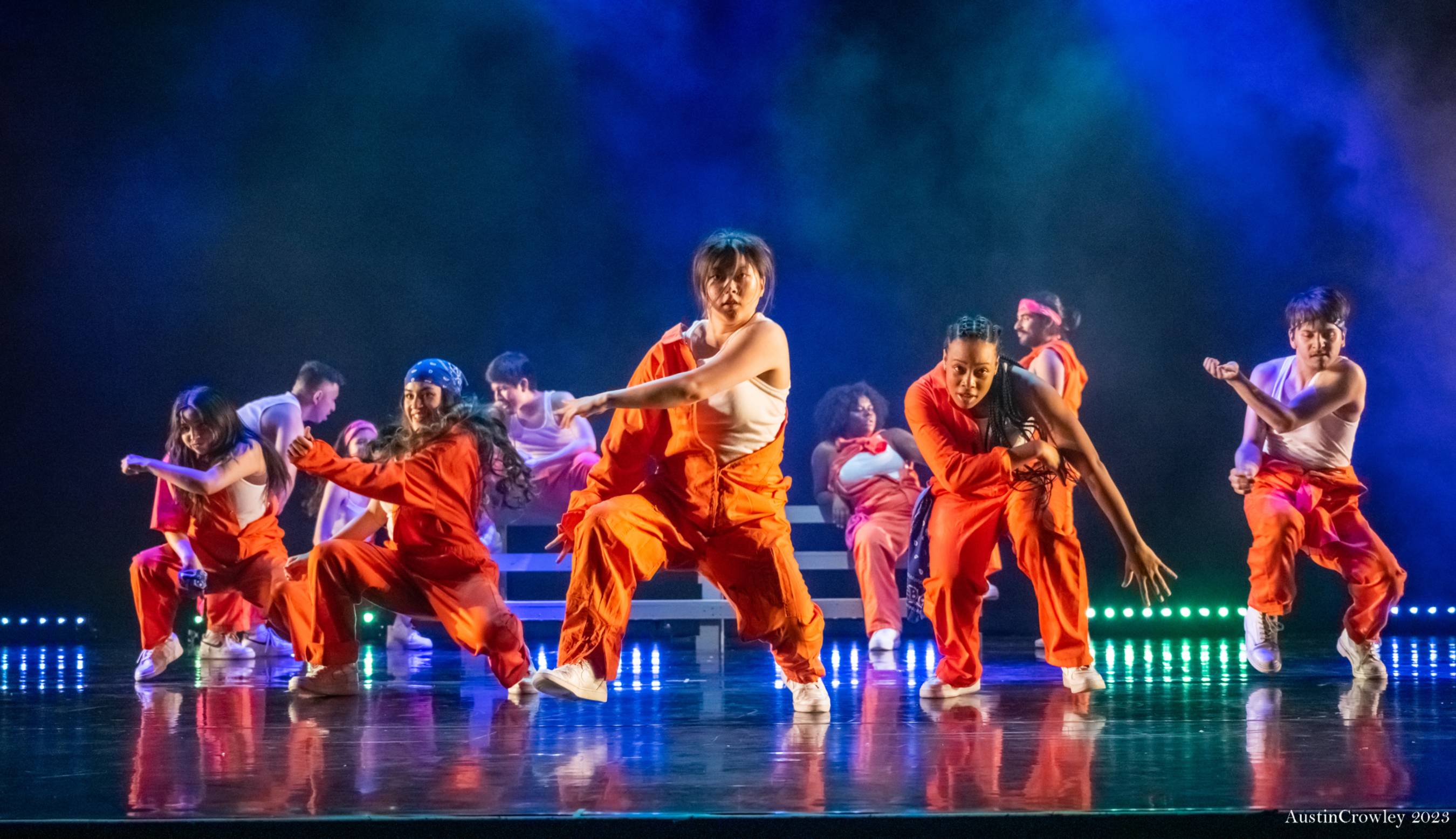 Dancers in orange jumpsuits step forward