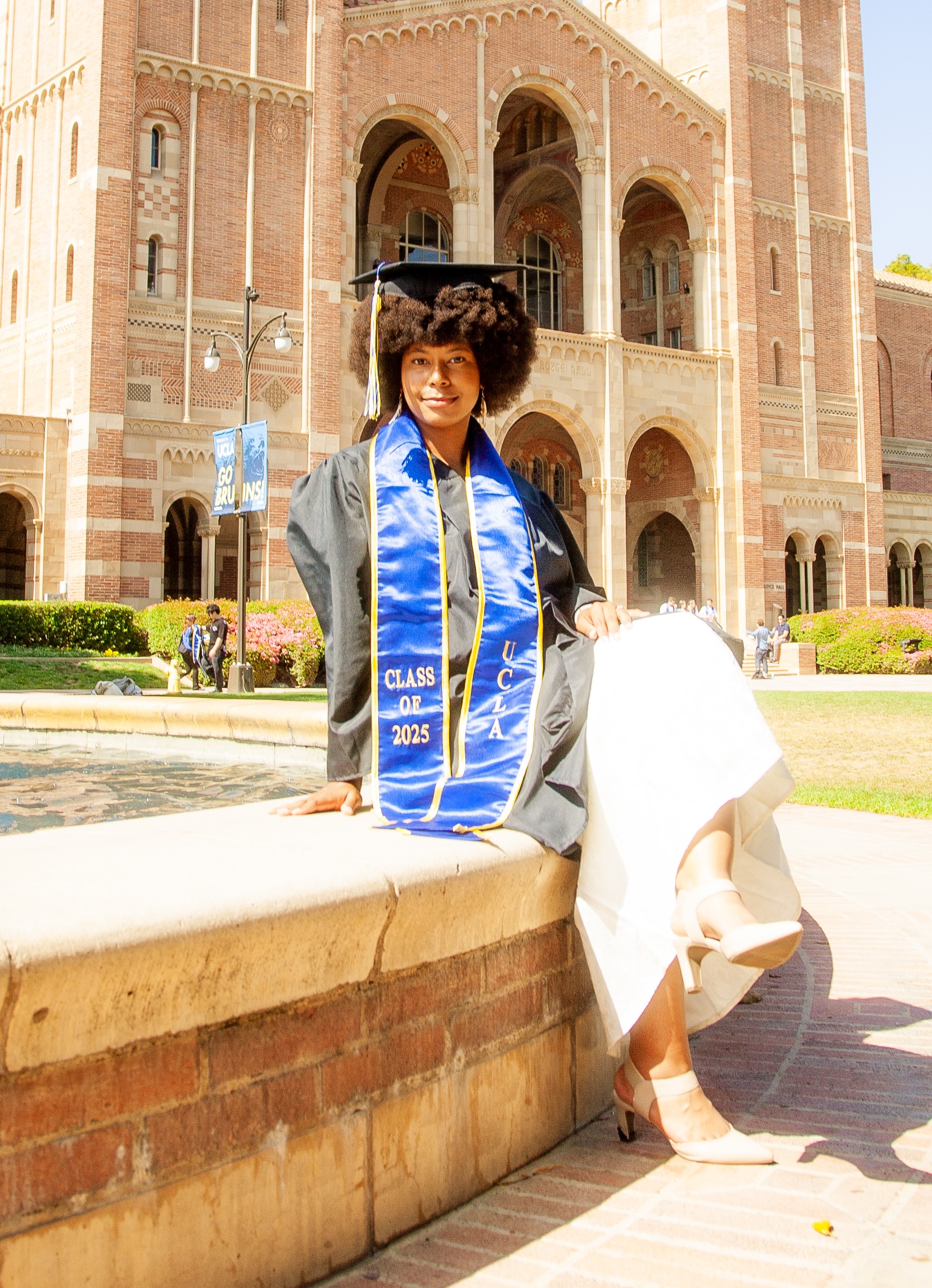 Laila wearing cap and gown sitting on fountain in front of UCLA