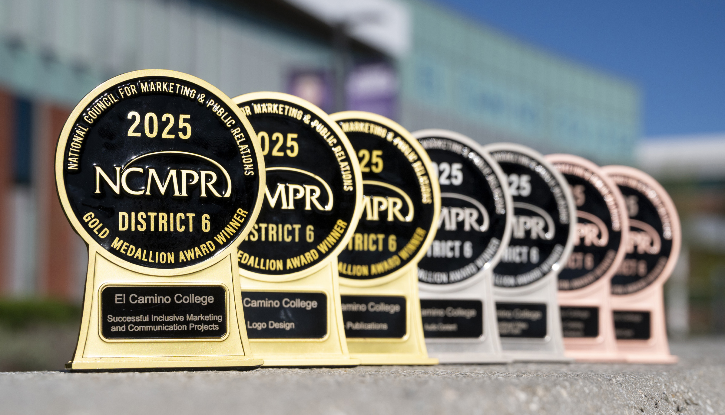 A row of NCMPR District 6 Medallion Awards—gold, silver, and bronze—displayed outdoors in front of a blurred campus building. The awards feature the El Camino College name and various winning categories.