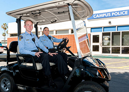 Two cadets driving in the courtesy shuttle in front of the Campus Police Station