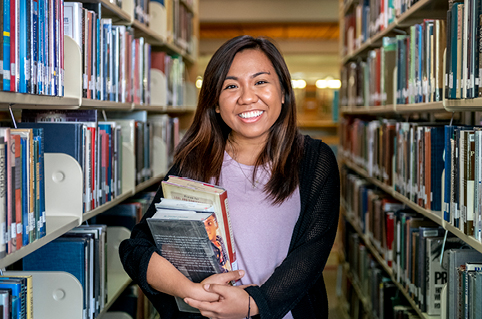 Student holds books in the library stacks.
