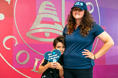 CARE student smiles with her son in front of pink and purple wall with ECC logo.